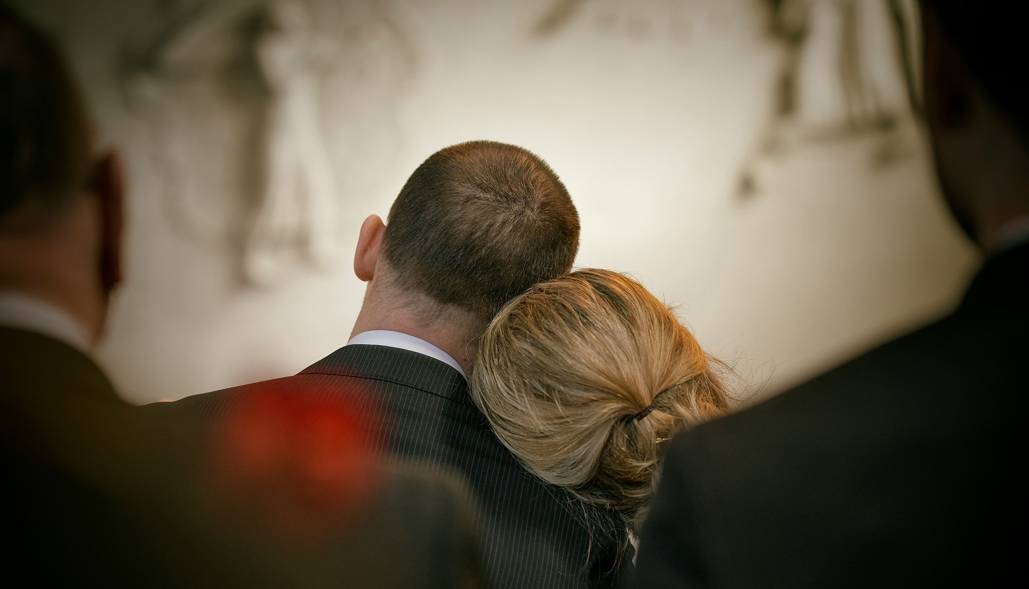 Couple sitting close together, with the woman's head resting on the man's shoulder, seen from behind.
