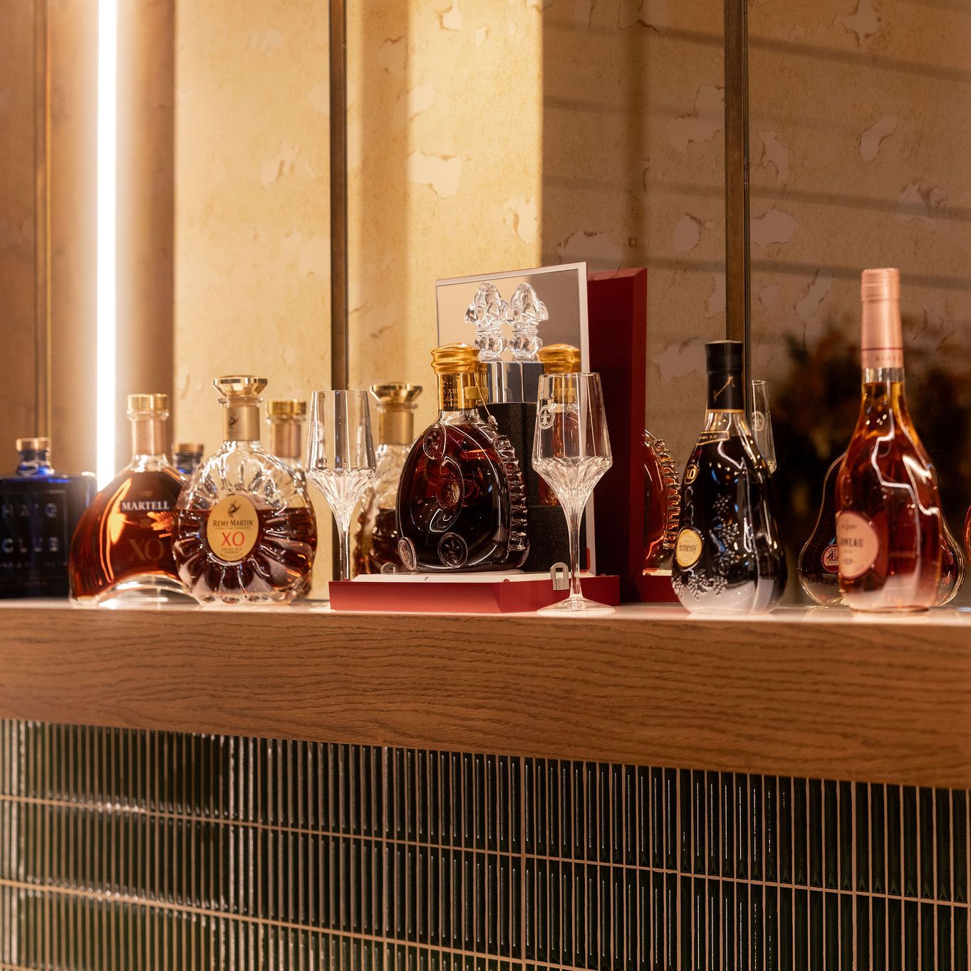 A collection of premium cognac and liquor bottles displayed on a wooden shelf with glassware.