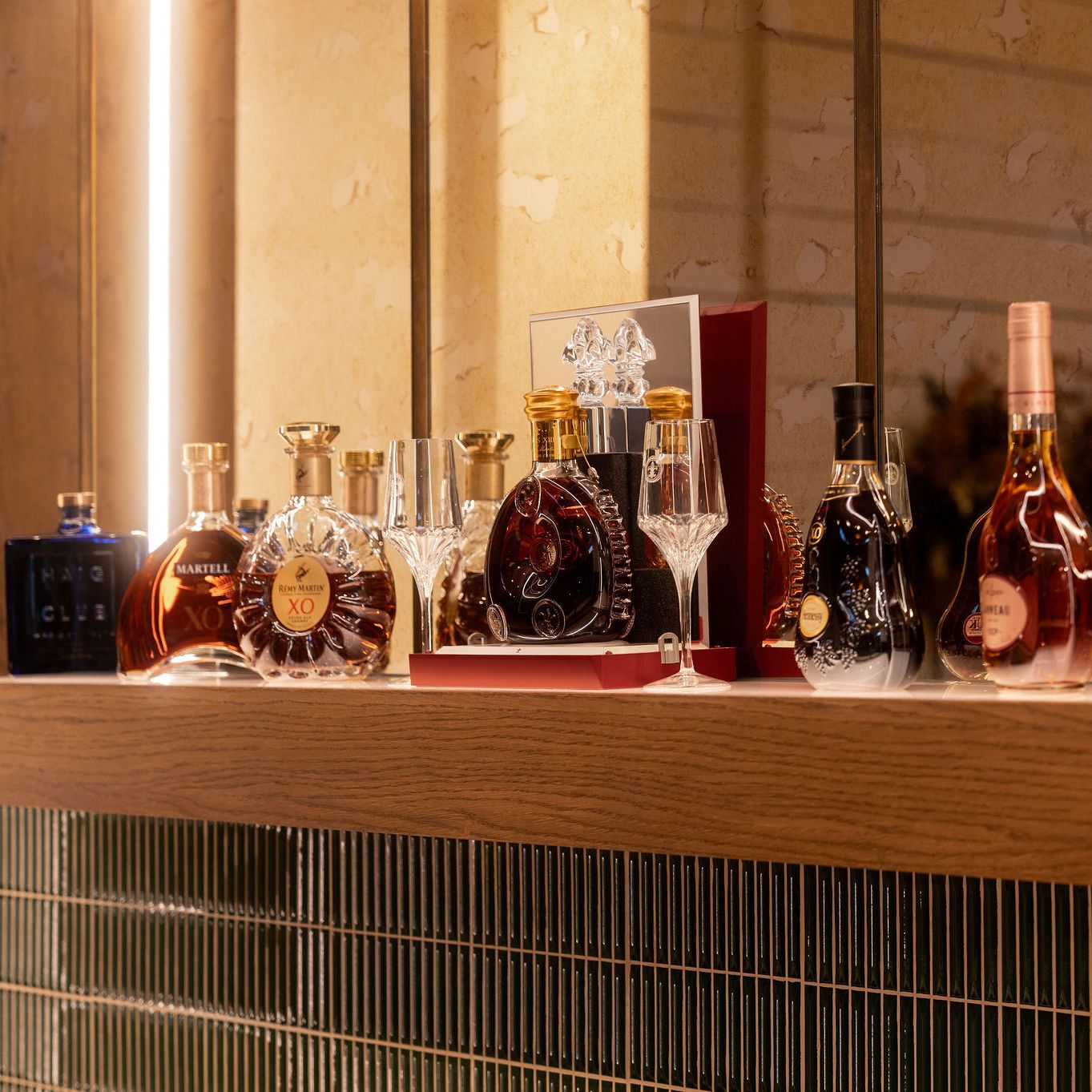 A collection of premium cognac and liquor bottles displayed on a wooden shelf with glassware.