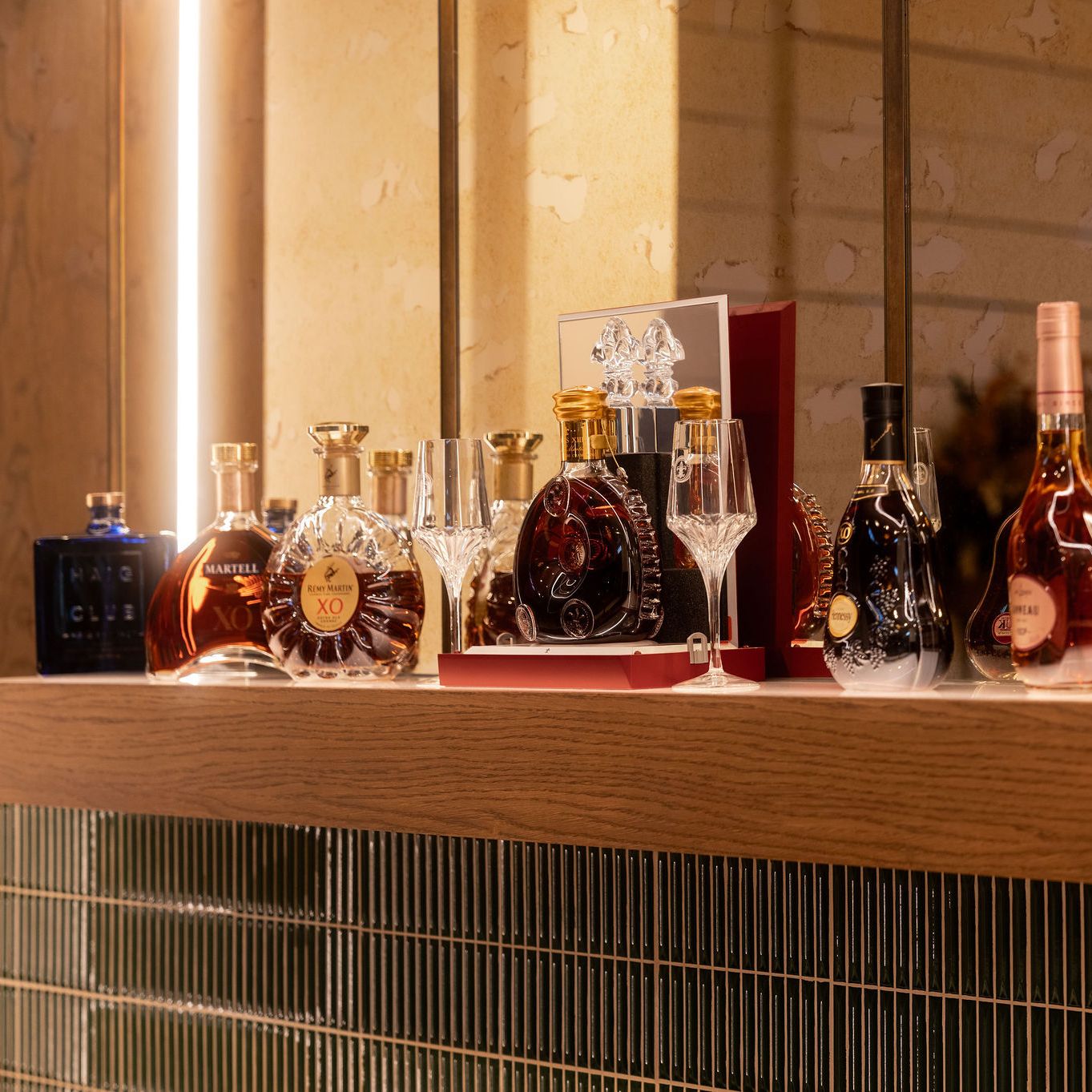 A collection of premium cognac and liquor bottles displayed on a wooden shelf with glassware.
