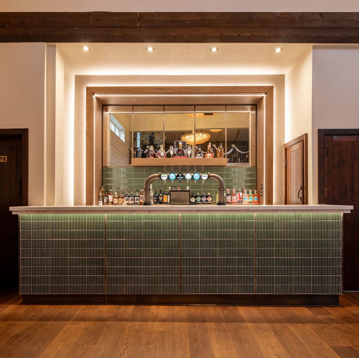Modern bar with green tile front, wooden accents, and bottles displayed behind the counter.