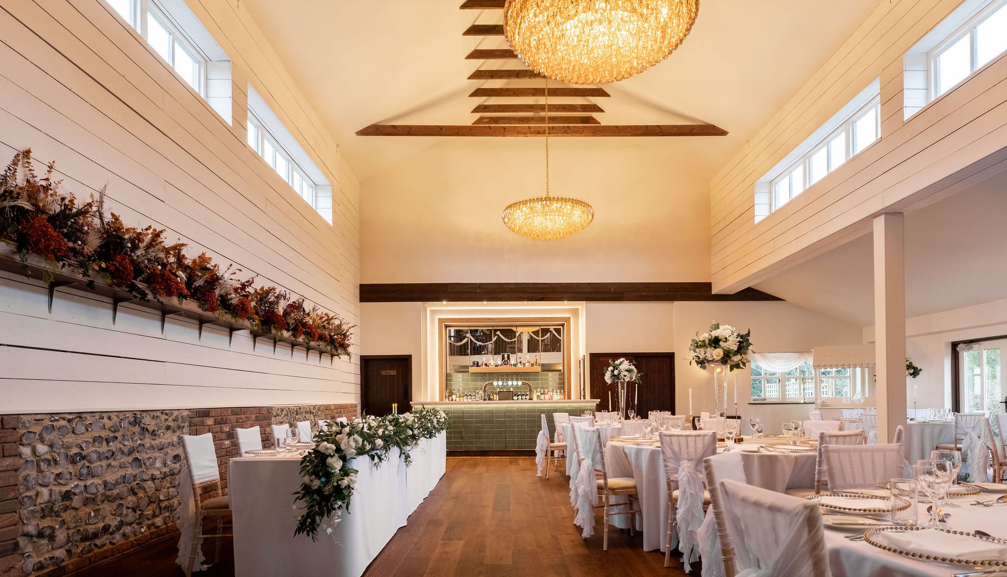 Elegant wedding reception venue with decorated tables, chandeliers, and a bar at the back