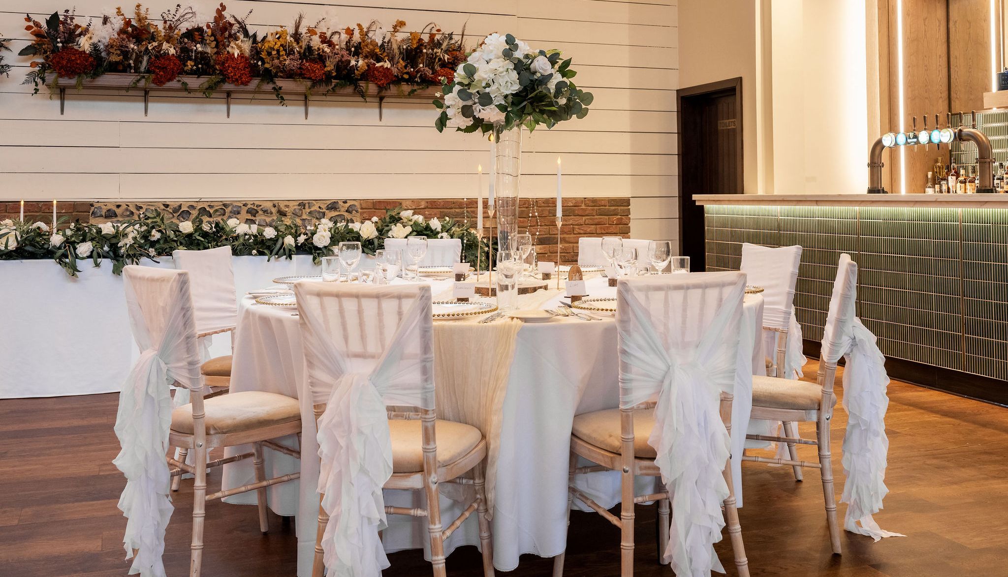Elegant wedding reception setup with round table, floral arrangements, and a large chandelier.