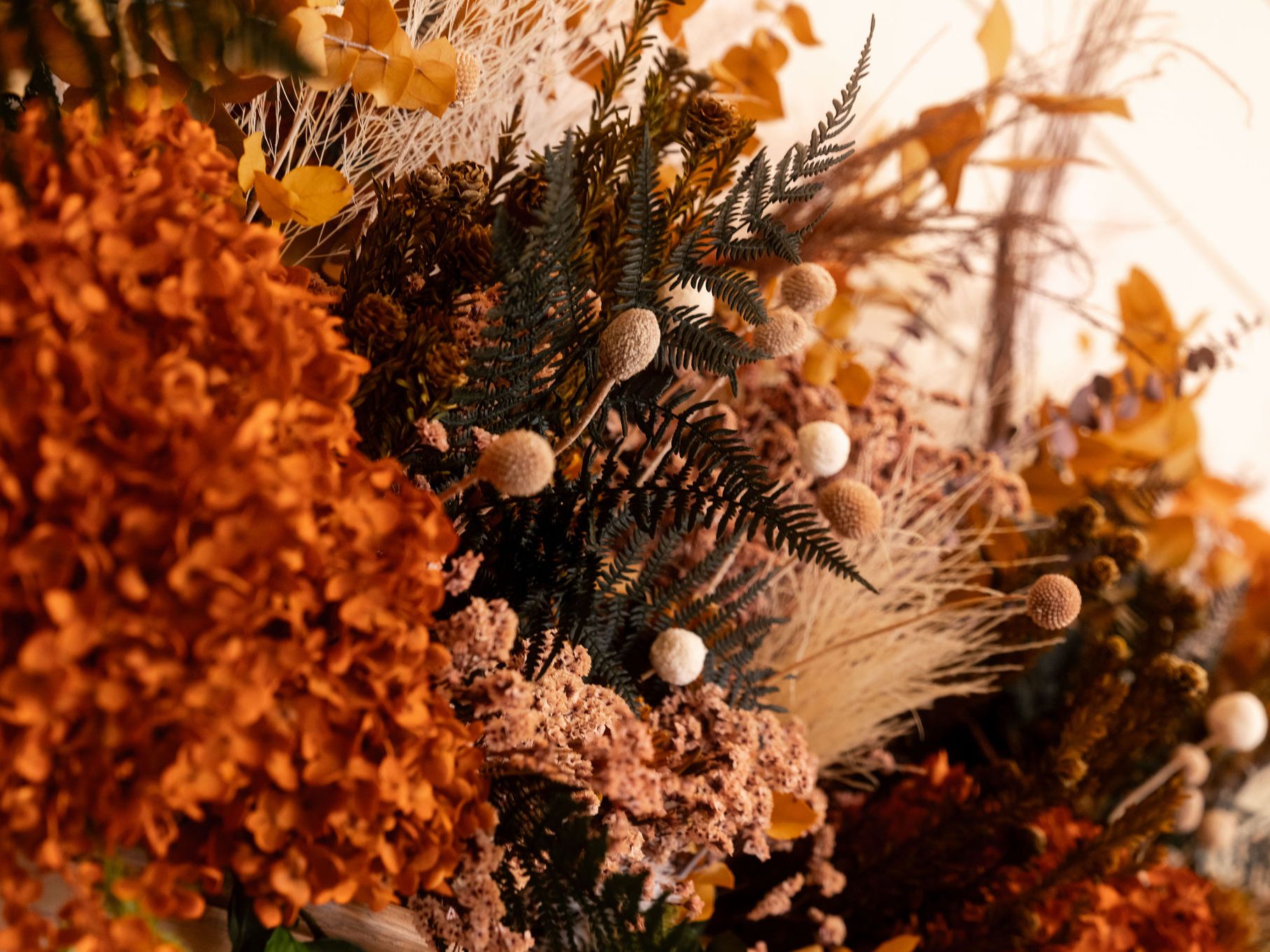 Close-up of a vibrant autumn floral arrangement with dried orange hydrangeas, ferns, and textured foliage.