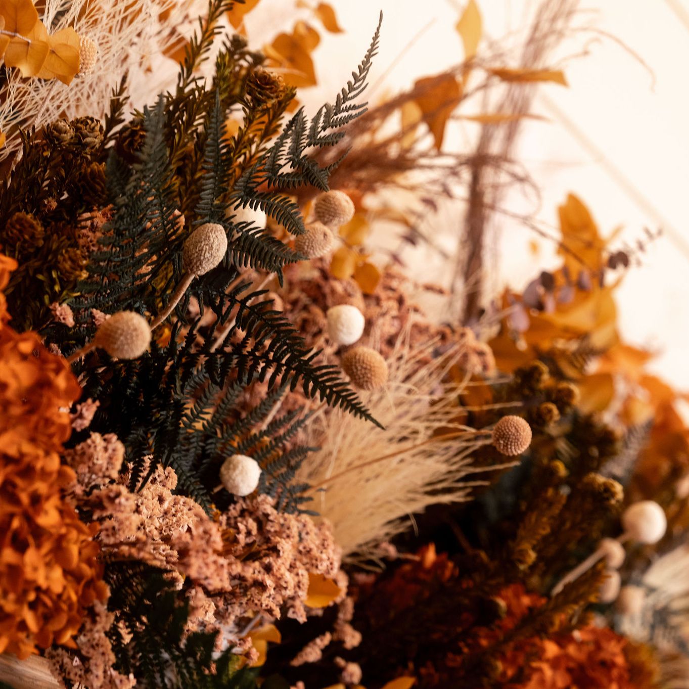 Close-up of a vibrant autumn floral arrangement with dried orange hydrangeas, ferns, and textured foliage.