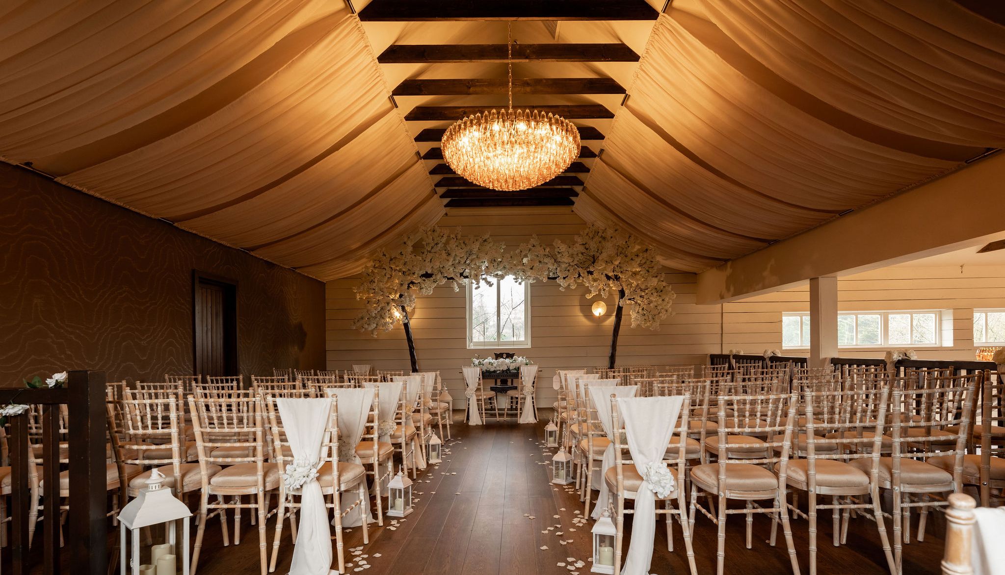 Elegant indoor wedding ceremony setup with rows of chairs, draped fabric ceiling, and a chandelier.