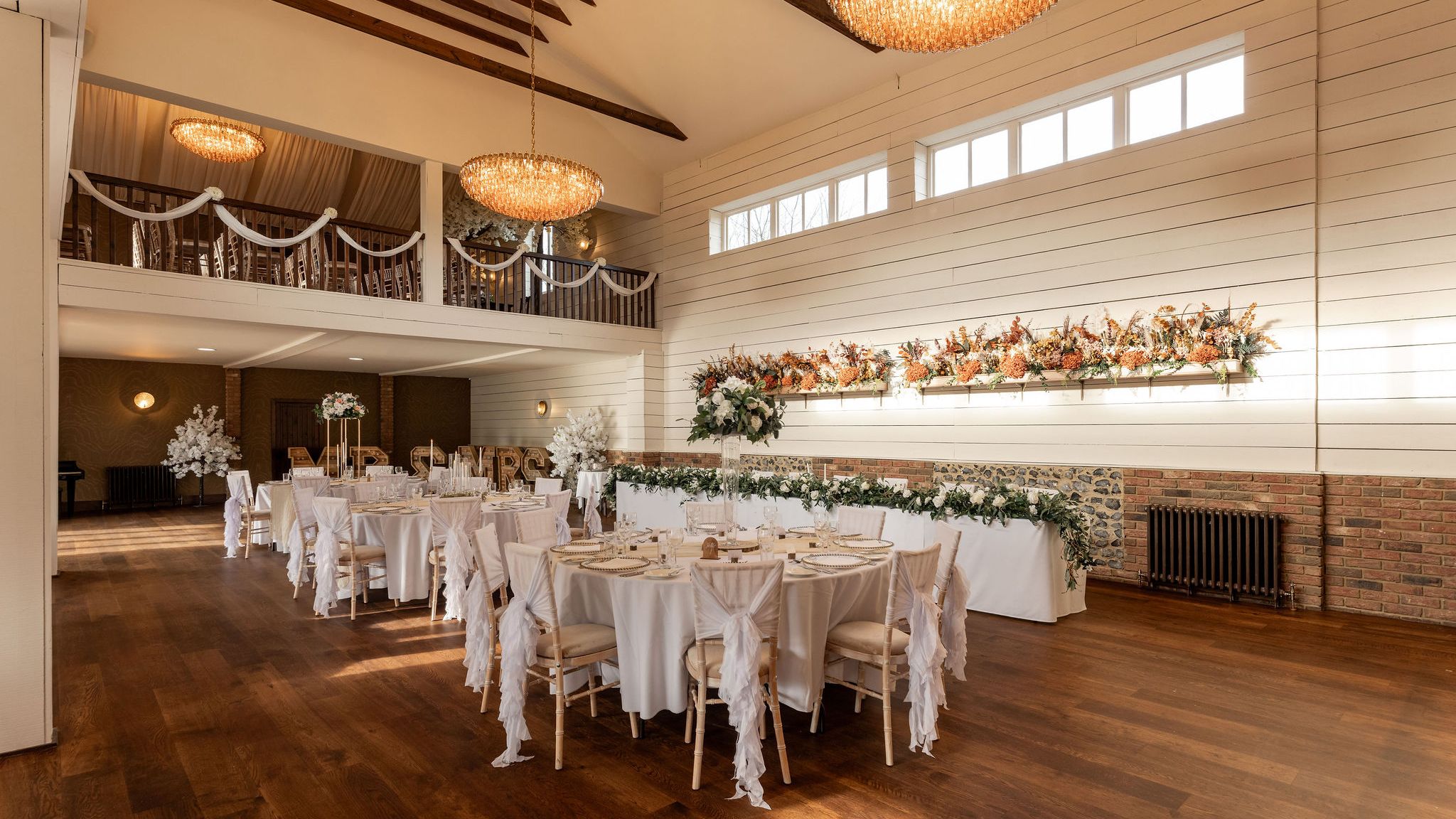 Elegant wedding reception hall with white decor, floral arrangements, and chandeliers