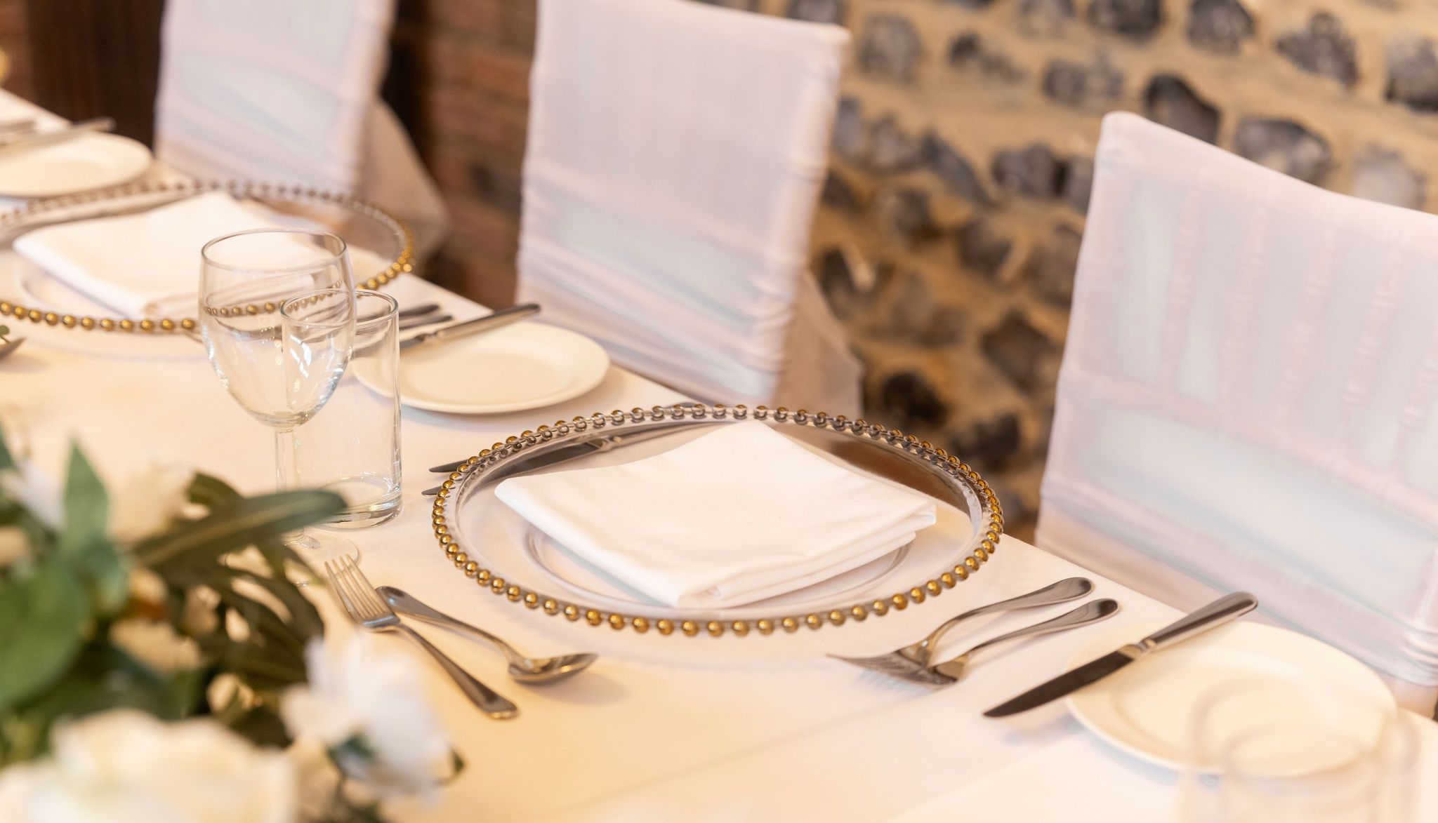 Elegant table setting with white linens, gold-rimmed charger plates, and folded napkins.