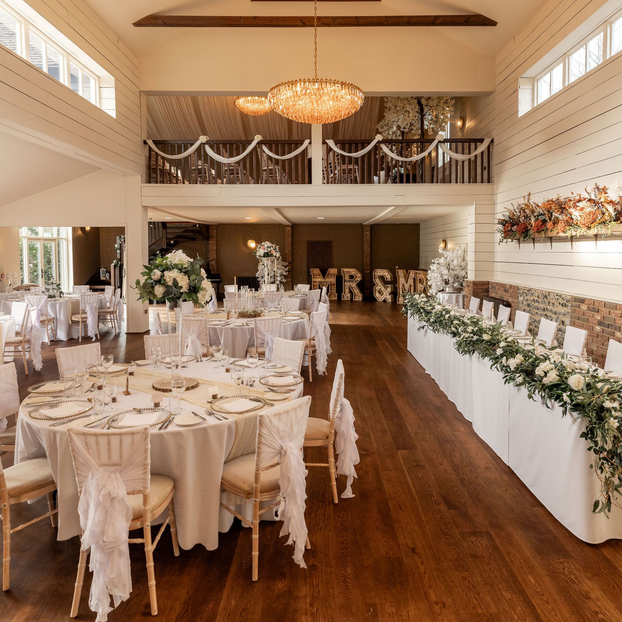 Elegant wedding reception dining hall with round tables, floral decorations, and chandeliers.