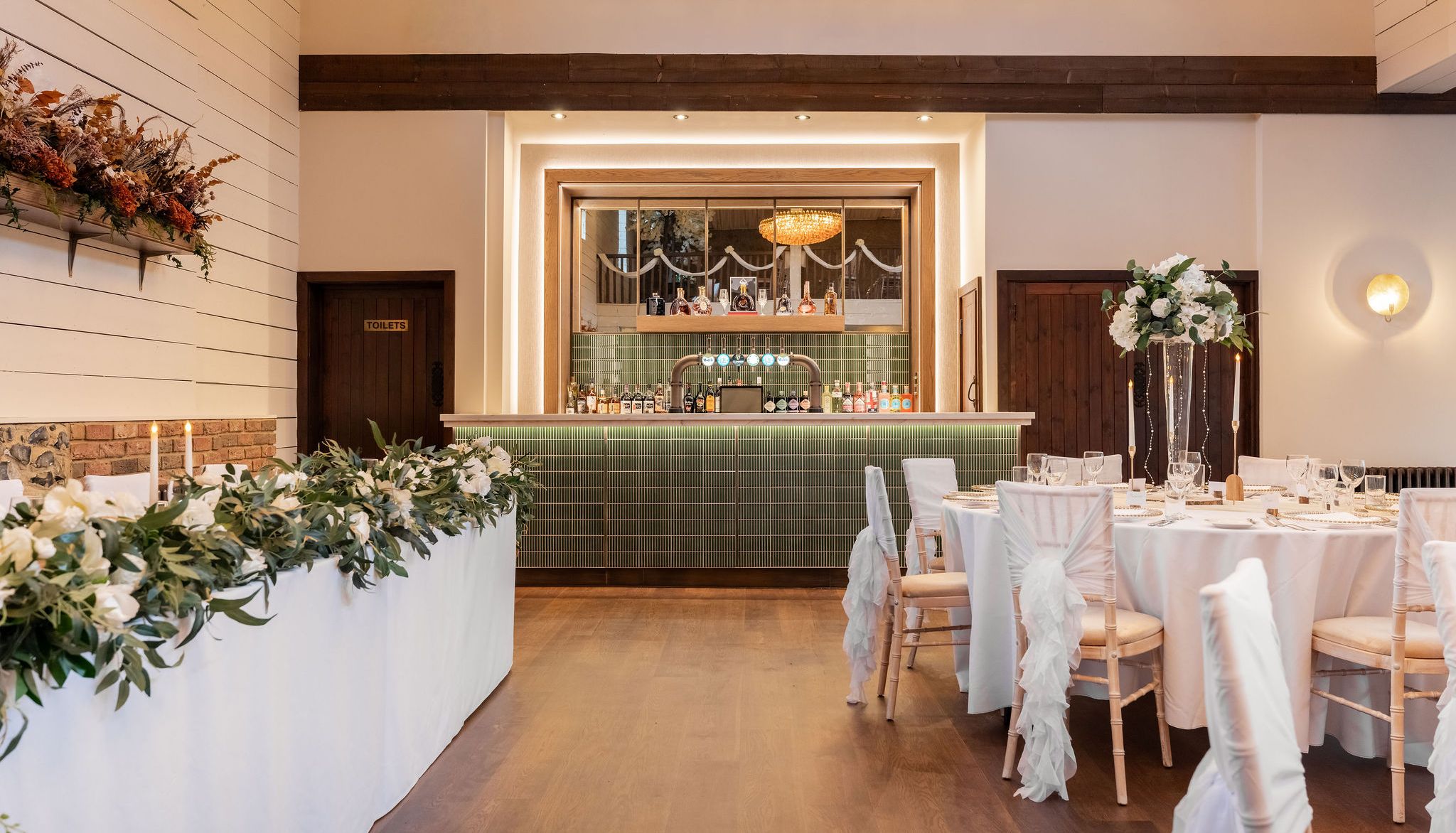 Elegant wedding reception room with a bar, floral arrangements, and decorated tables