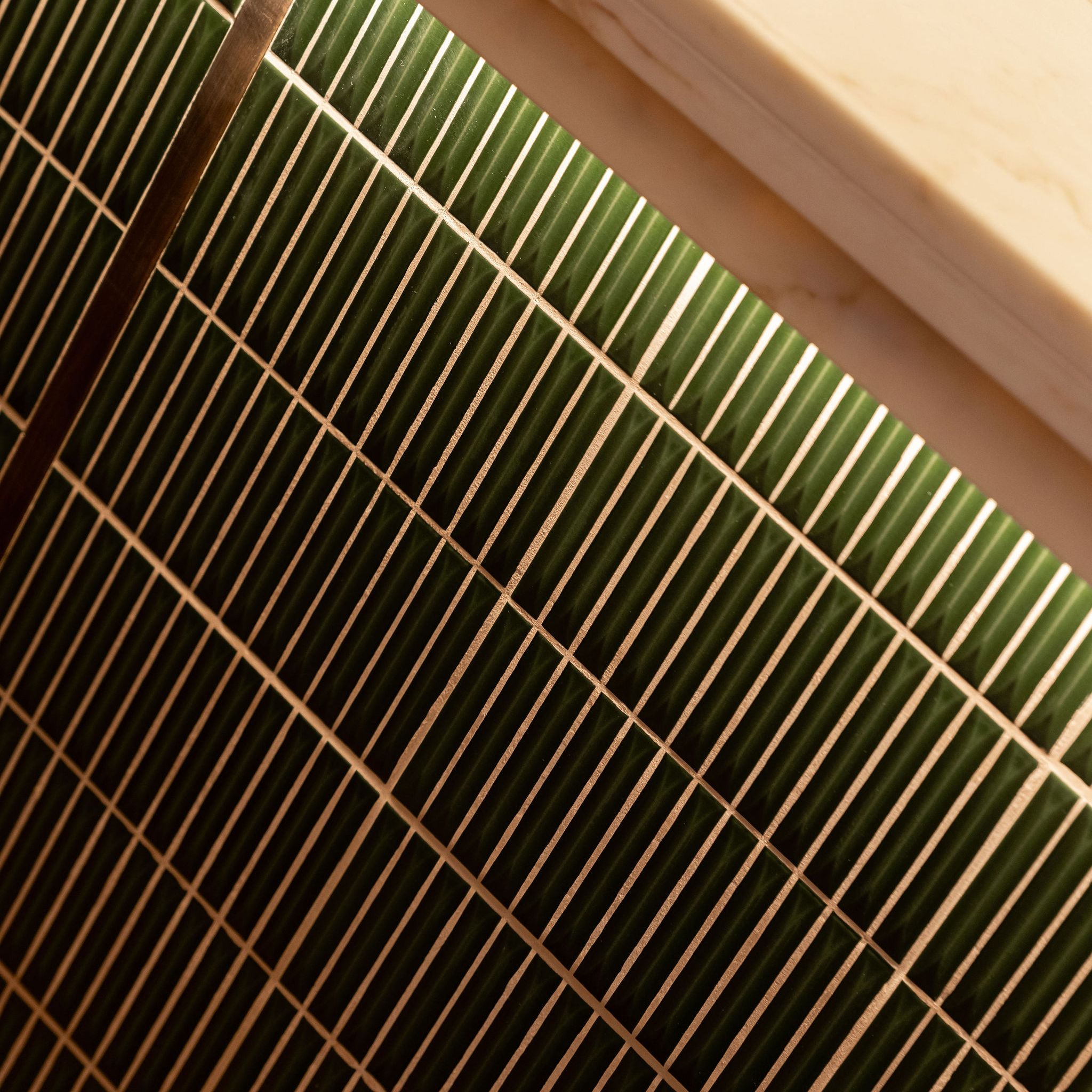 Close-up view of green rectangular tiles with white grout beneath a marble countertop
