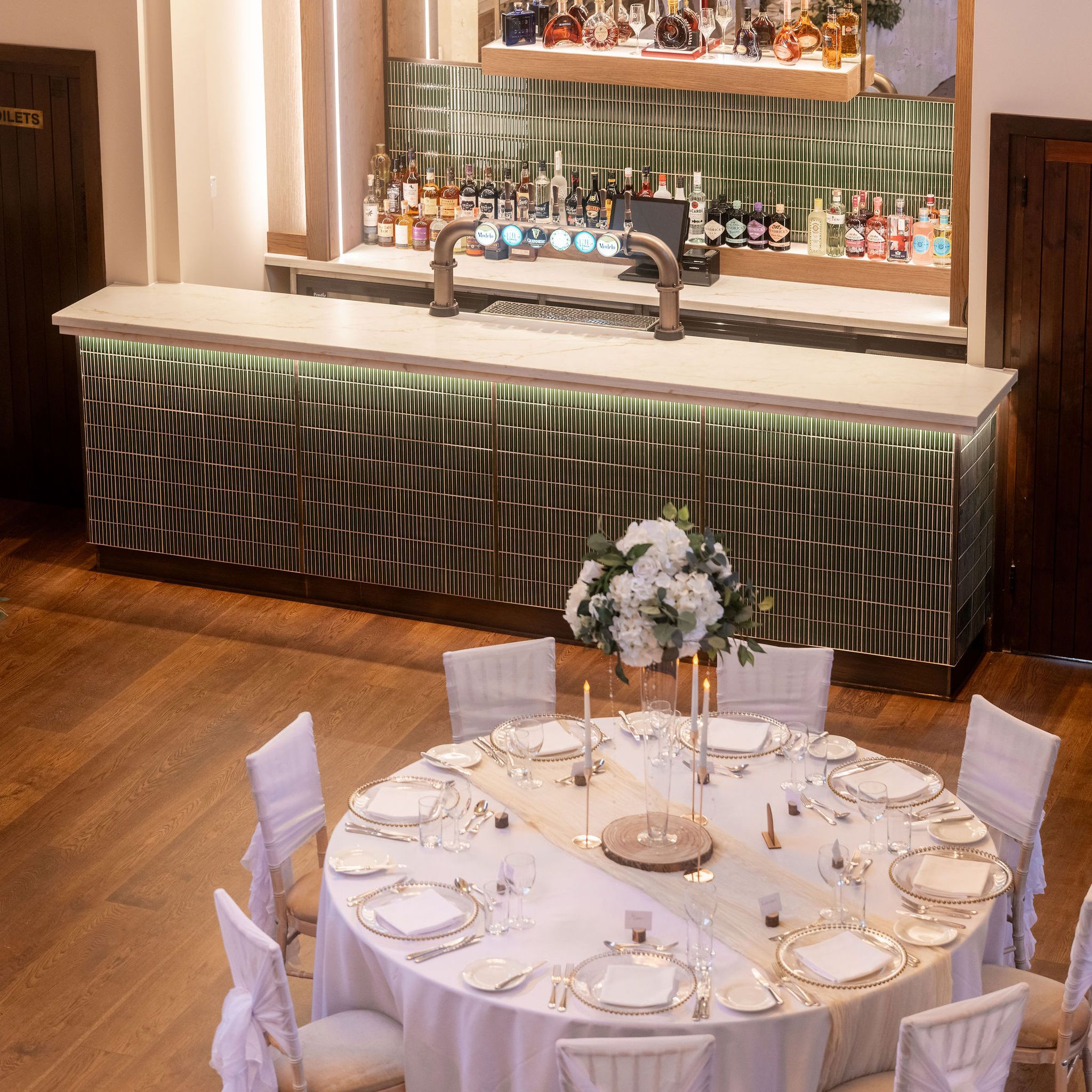 Elegant bar and banquet table setup under a large chandelier in a sophisticated venue.