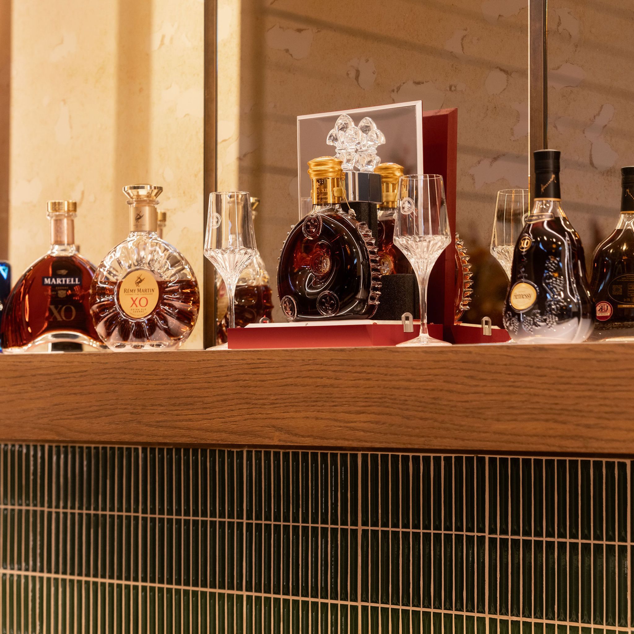 A selection of premium cognac bottles and crystal glasses displayed on a wooden shelf.