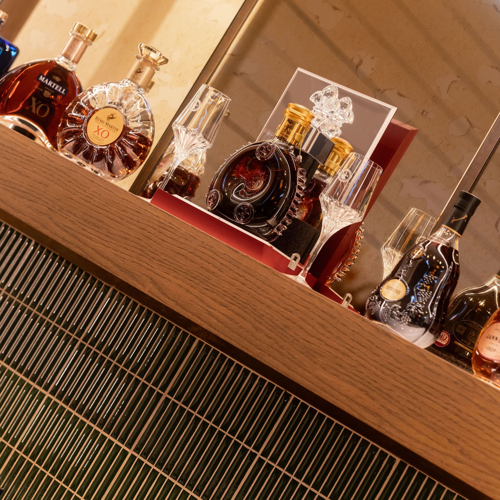 A selection of premium cognac bottles and elegant glassware displayed on a wooden bar shelf.