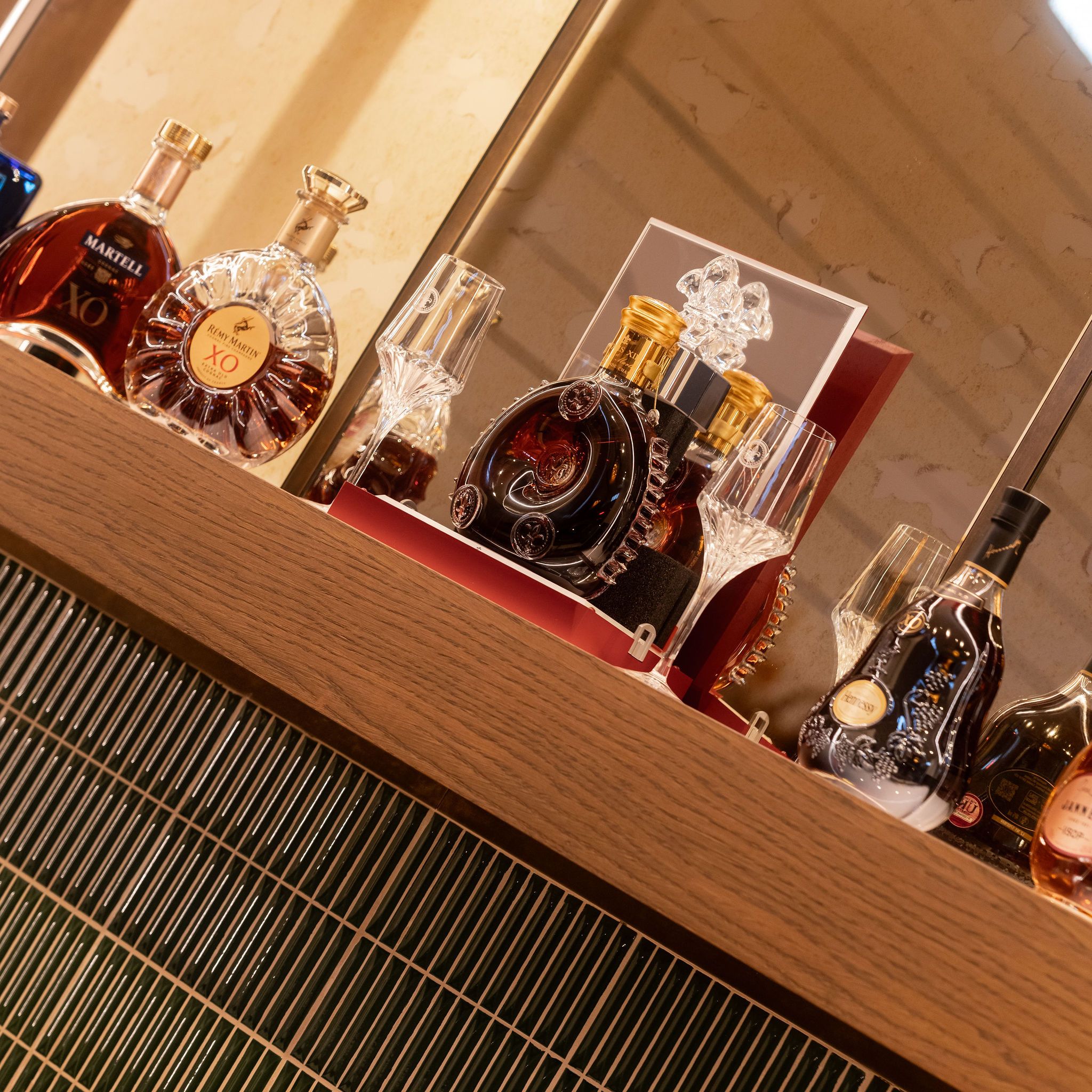 A selection of premium cognac bottles and elegant glassware displayed on a wooden bar shelf.
