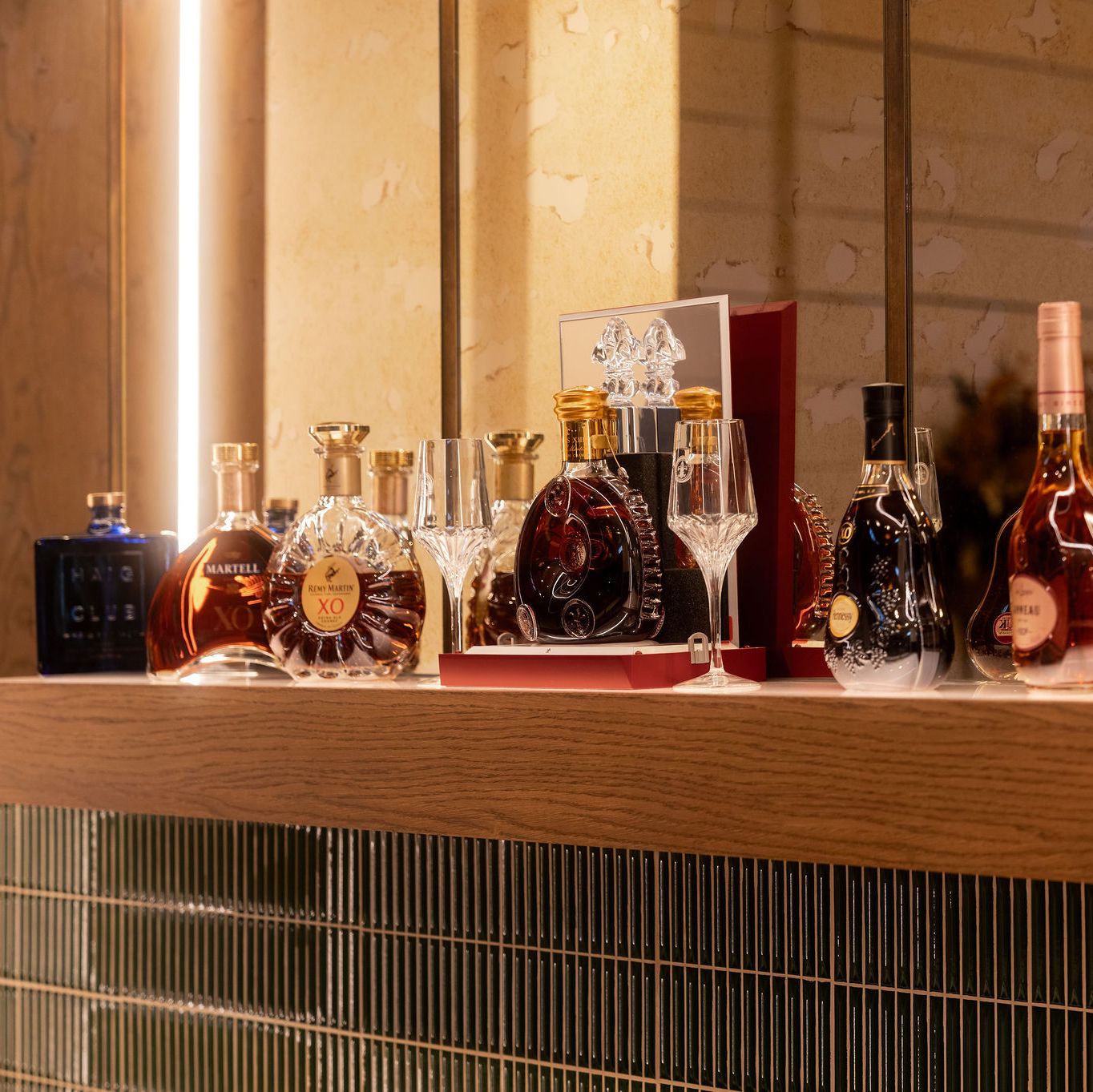 A selection of premium cognac and liquor bottles displayed on a wooden shelf with glassware.