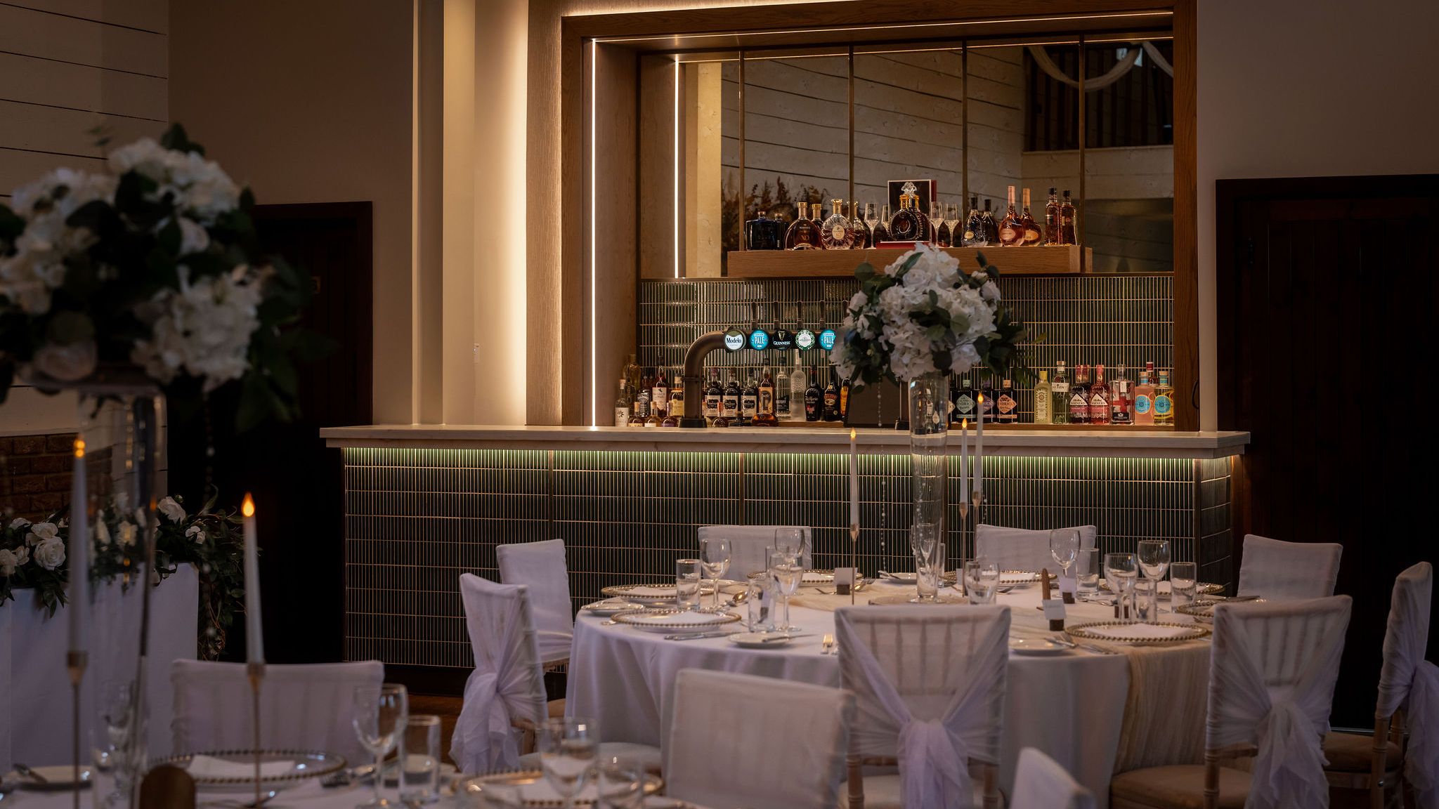 Elegant evening bar setup with formal dining tables decorated with white flowers and candles