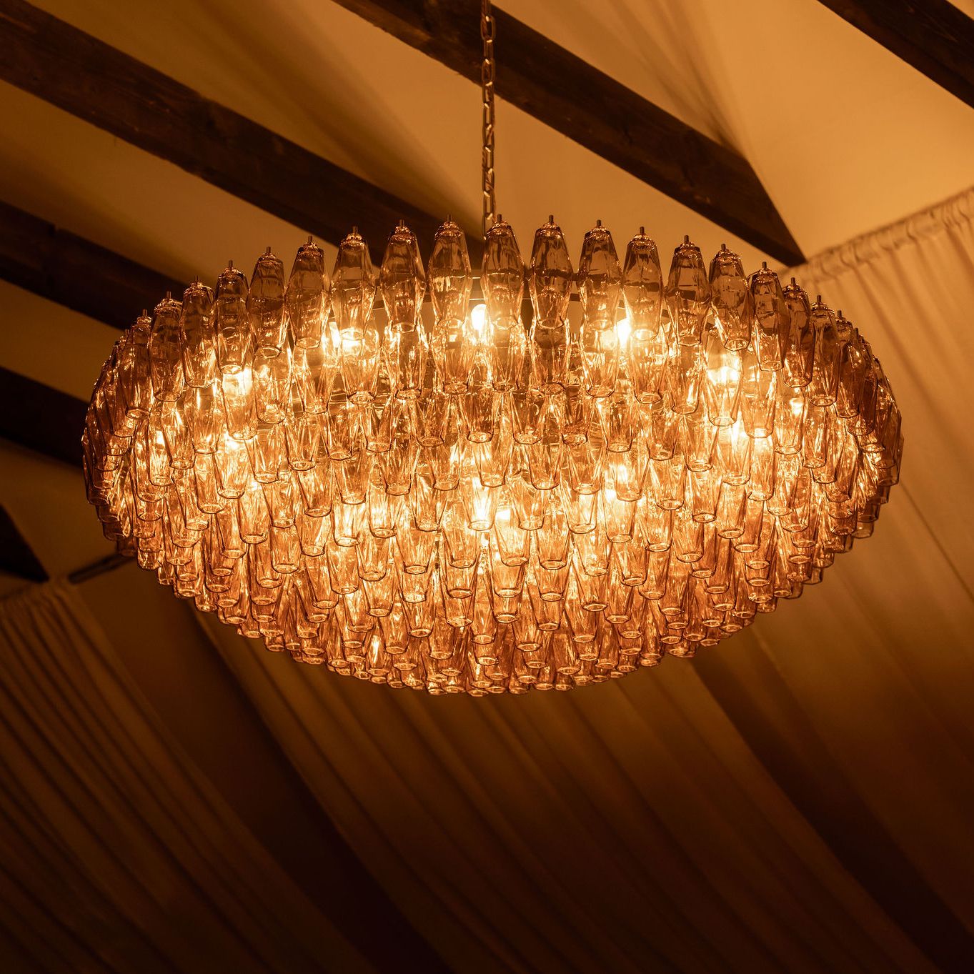 Elegant glass chandelier hanging from a ceiling with wooden beams