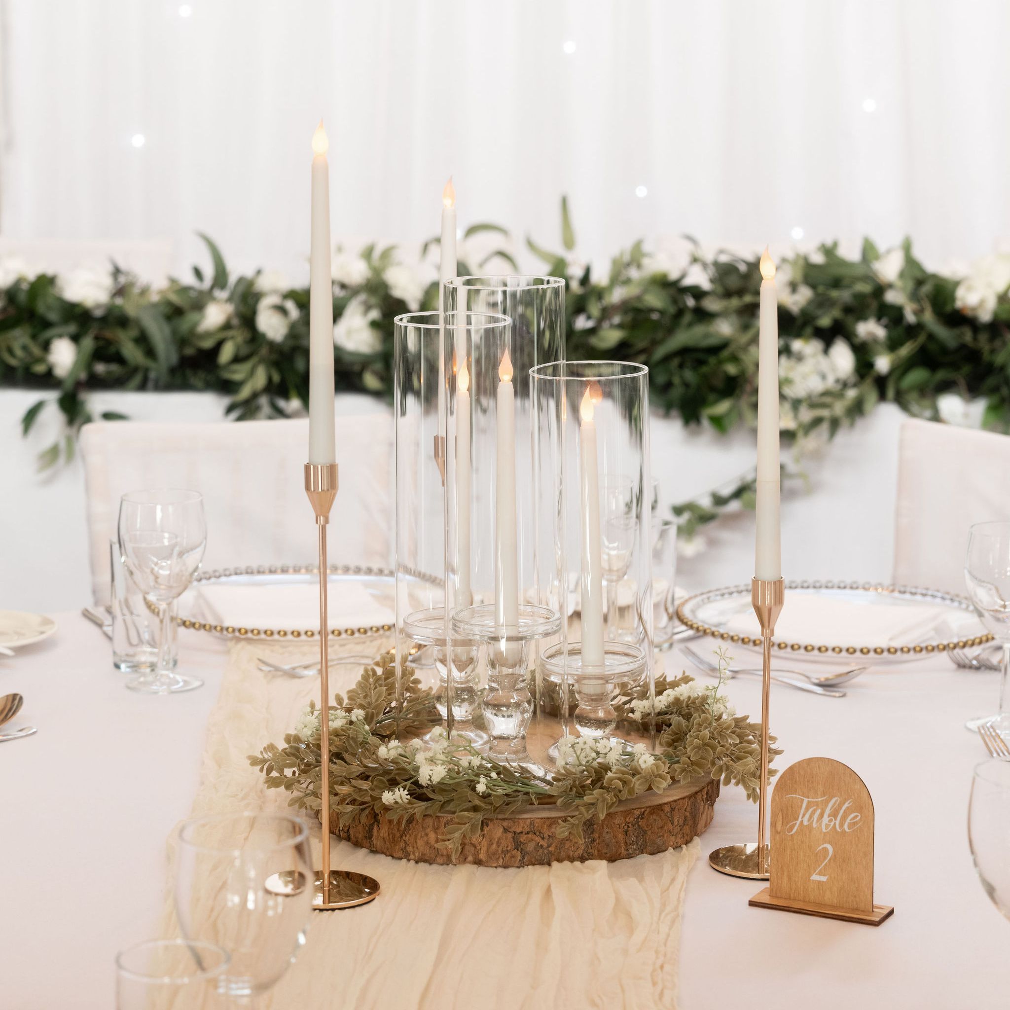 Elegant wedding table centerpiece with candles, greenery, and a Table 2 sign