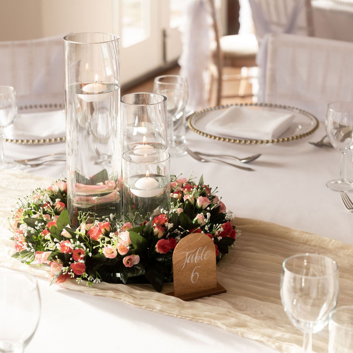 Elegant wedding table setting with glass candle holders, floral centerpiece, and table number 6.