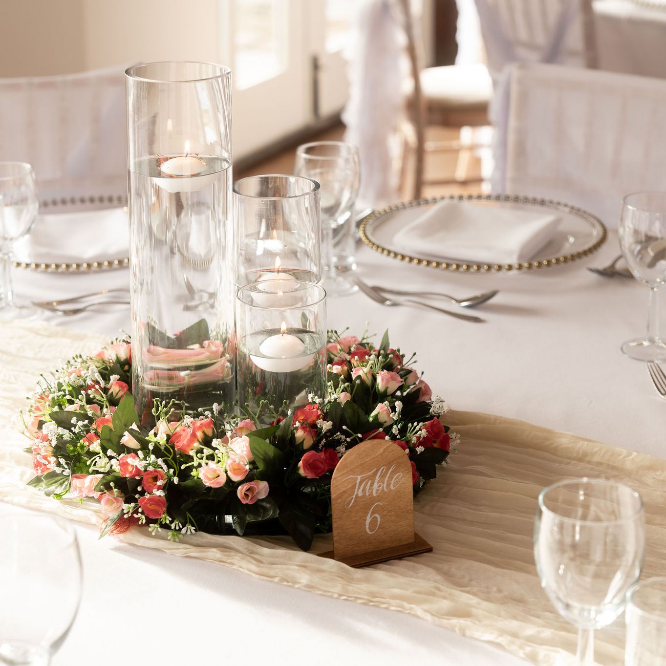 Elegant wedding table setting with glass candle holders, floral centerpiece, and table number 6.