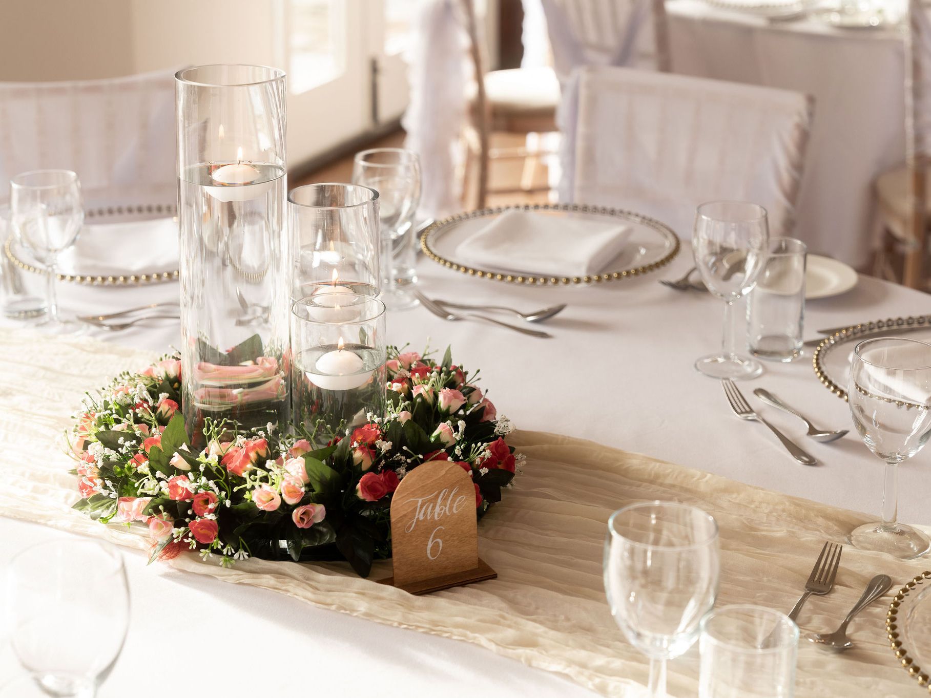 Elegant wedding table setting with glass candle holders, floral centerpiece, and table number 6.