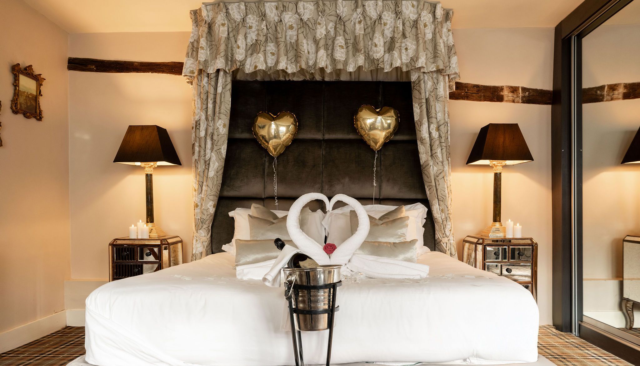 Romantic wedding suite with heart-shaped towel swans on the bed, champagne, and gold heart balloons.