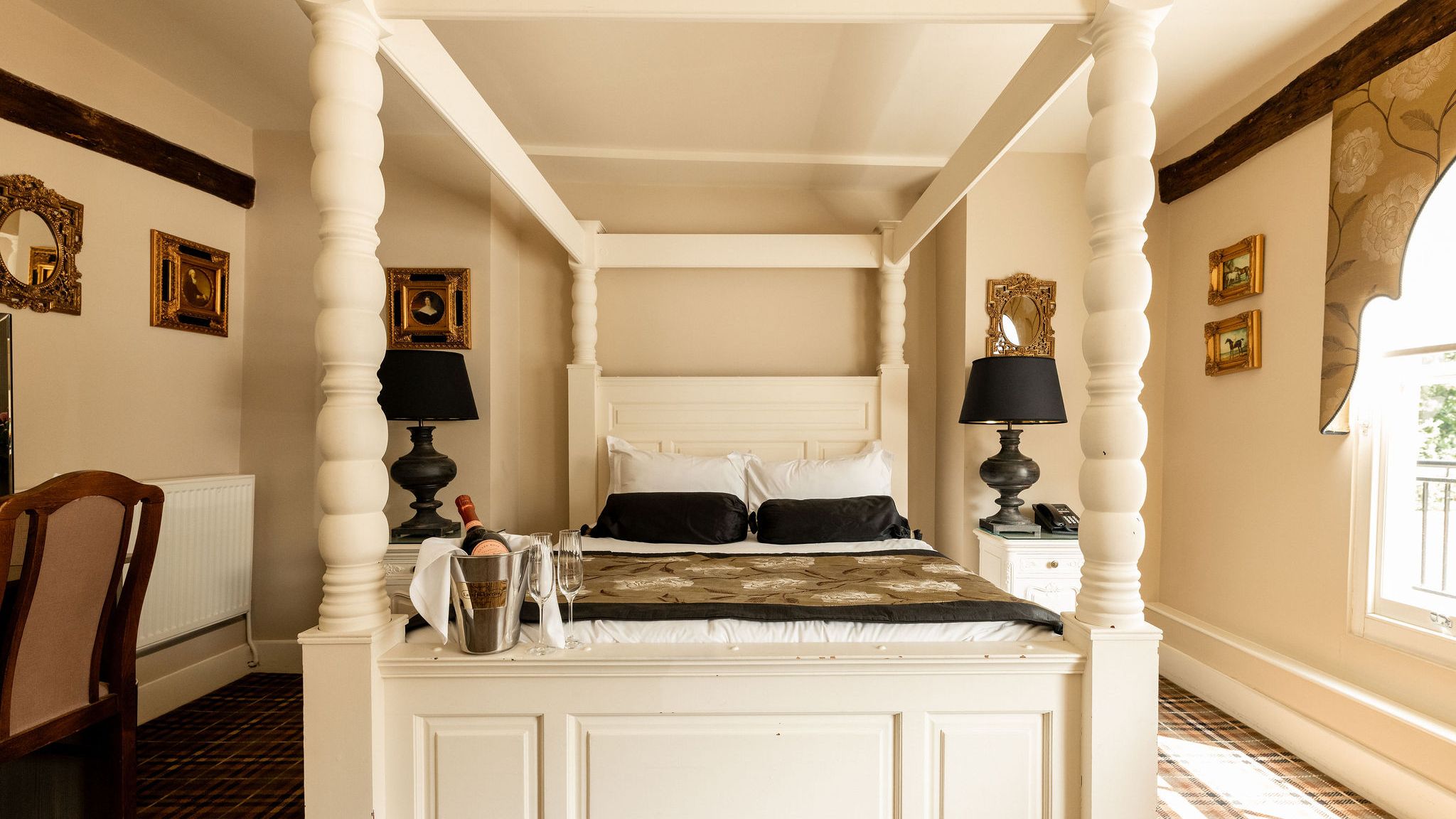 Elegant bedroom with a four-poster bed, bedside lamps, and champagne on the bed.