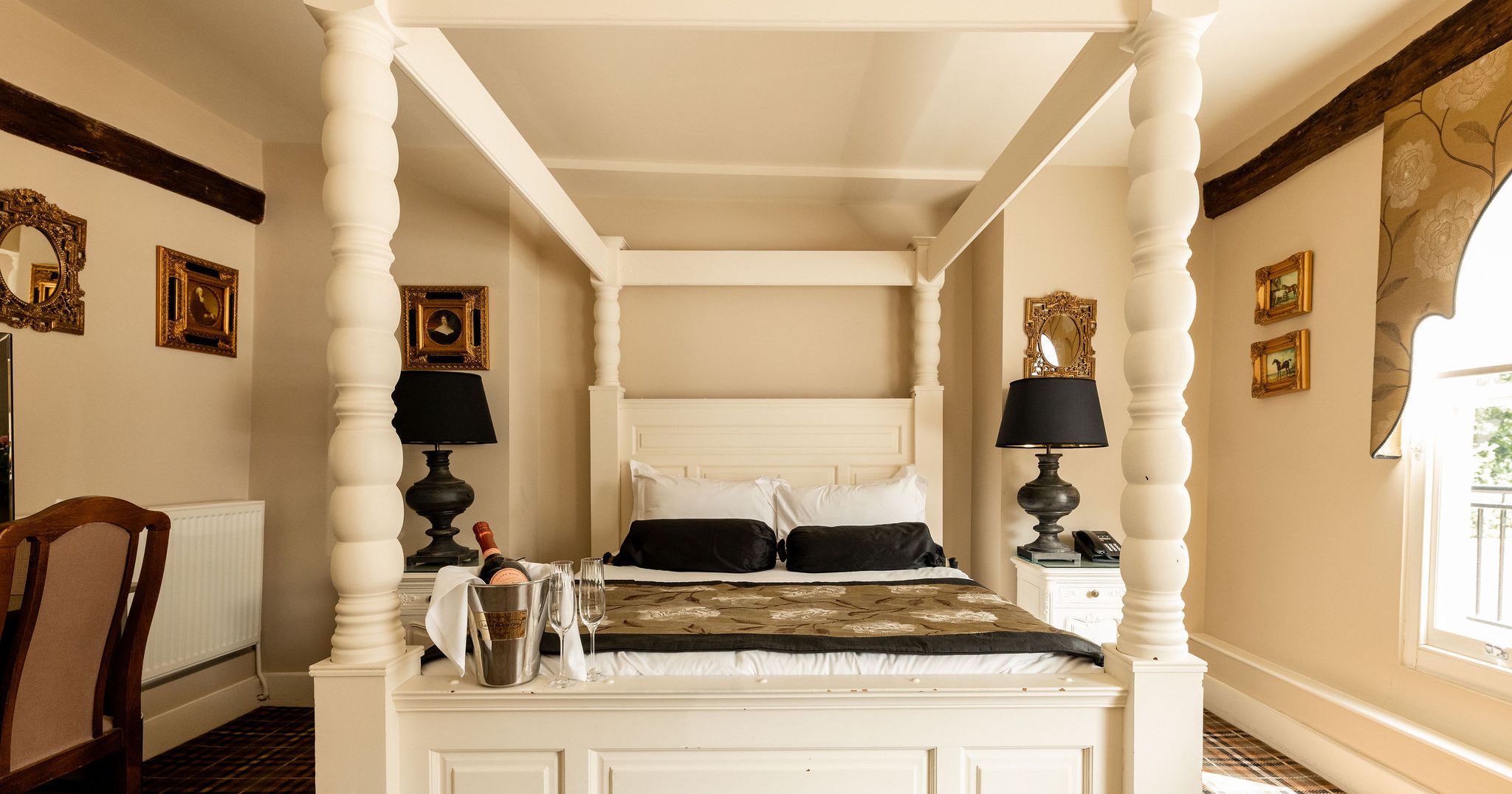 Elegant bedroom with a four-poster bed, bedside lamps, and champagne on the bed.