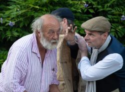 Two men engaged in a lively conversation outdoors with a green leafy background.