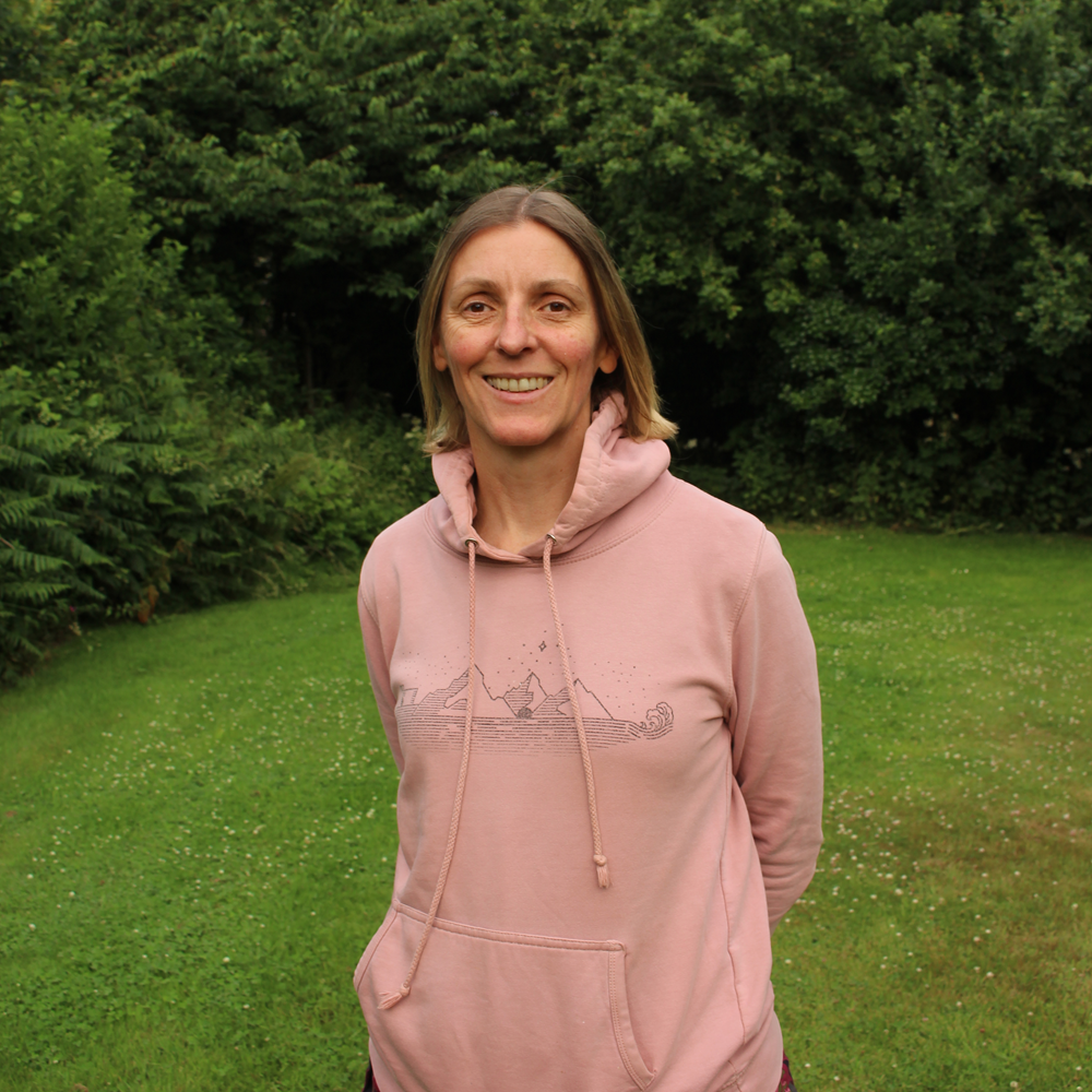 Person standing on grass wearing a pink hoodie with trees in the background