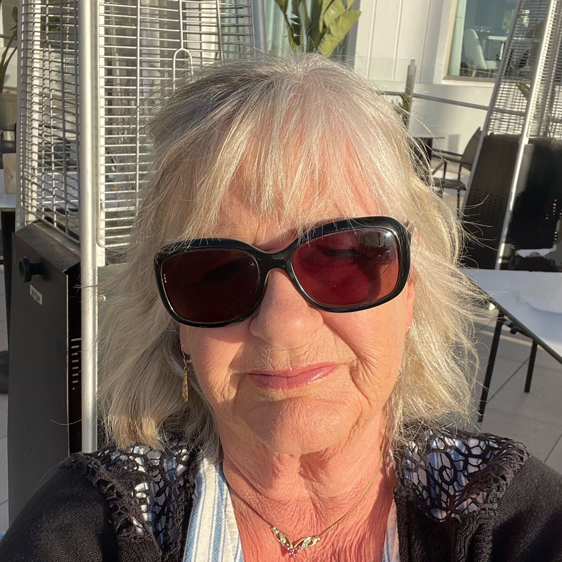 Older woman with light hair wearing dark sunglasses taking a selfie outdoors
