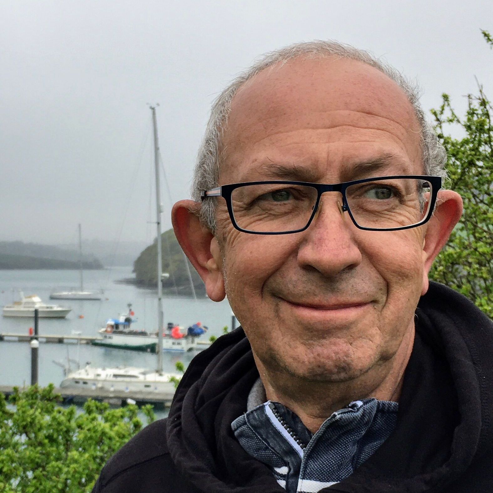 Older man with glasses smiling in front of a marina with boats