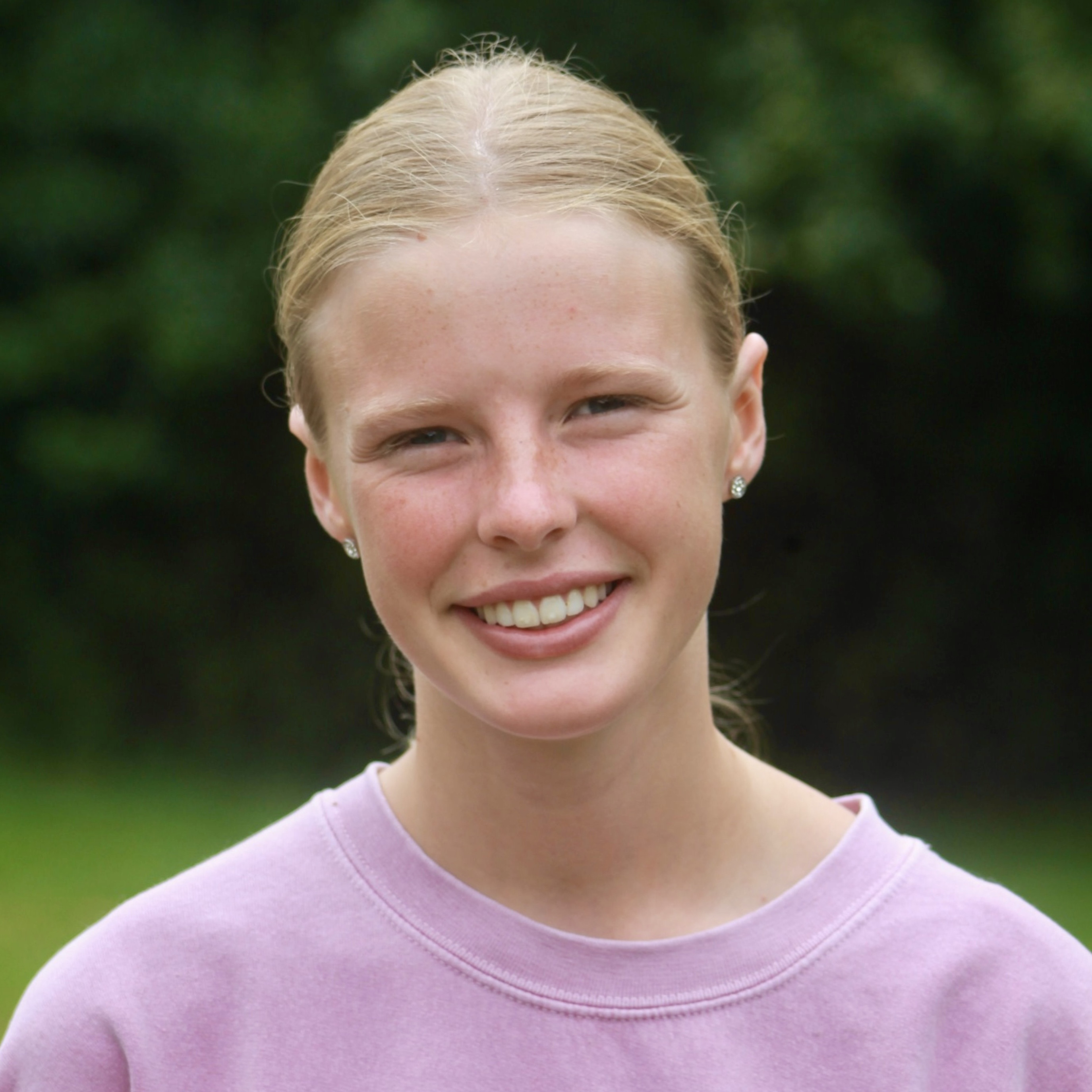 Smiling young person with blonde hair wearing a light purple sweater outdoors