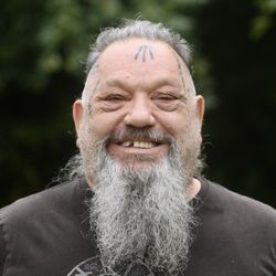 Smiling older man with facial tattoos and a long gray beard.