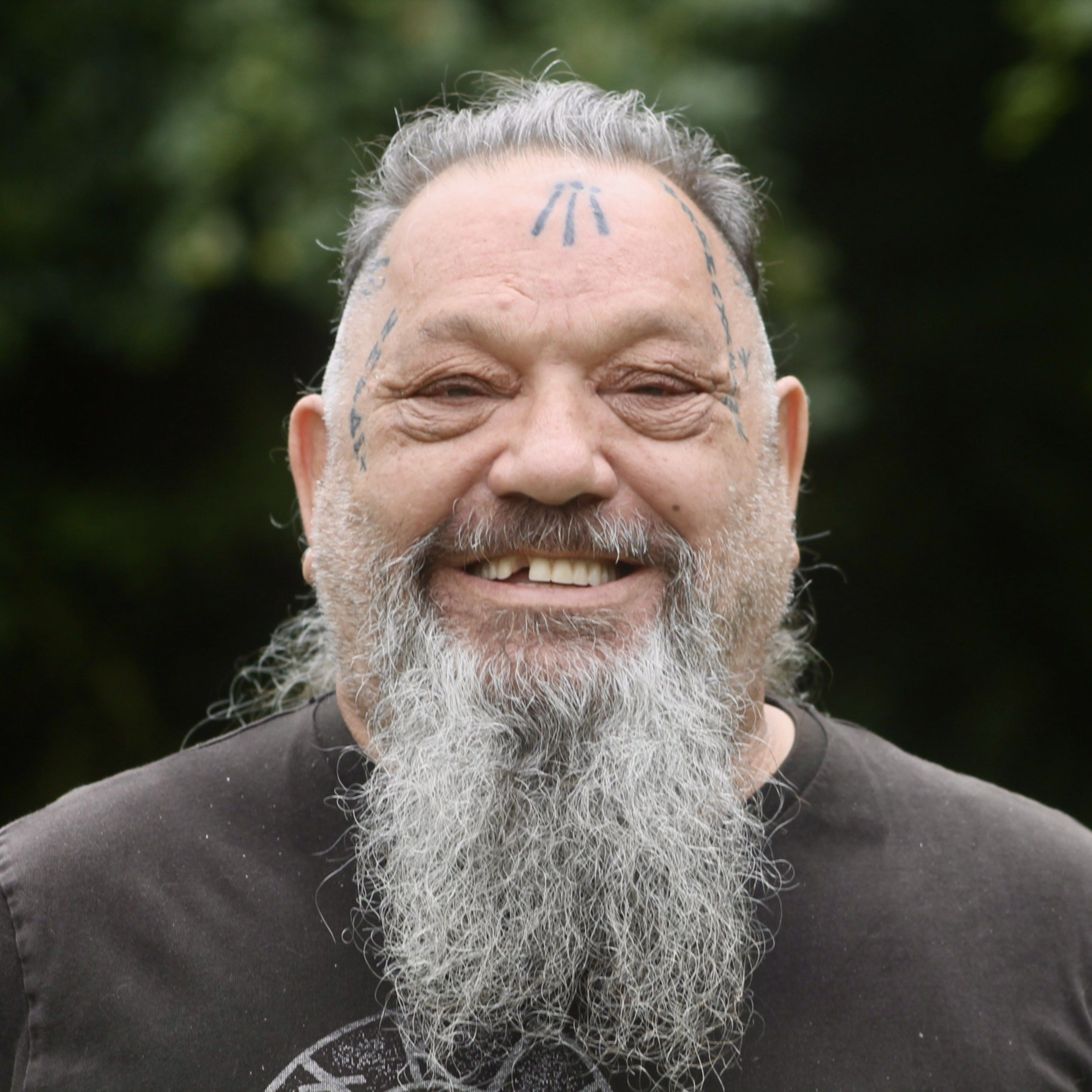 Smiling older man with facial tattoos and a long gray beard.