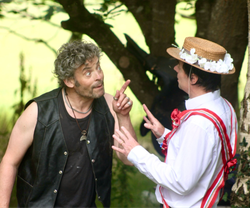 Two men having an animated conversation, one wearing a black leather vest and the other in a straw hat with flowers and a white shirt with red sash.