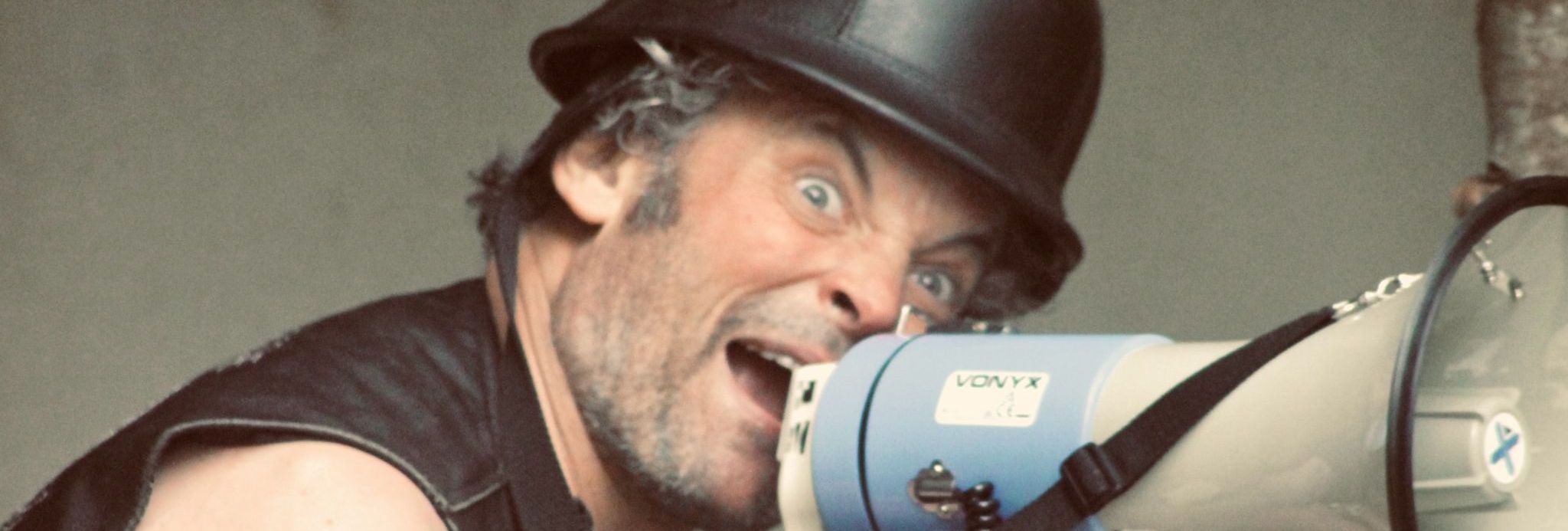 Man with a black helmet shouting into a megaphone