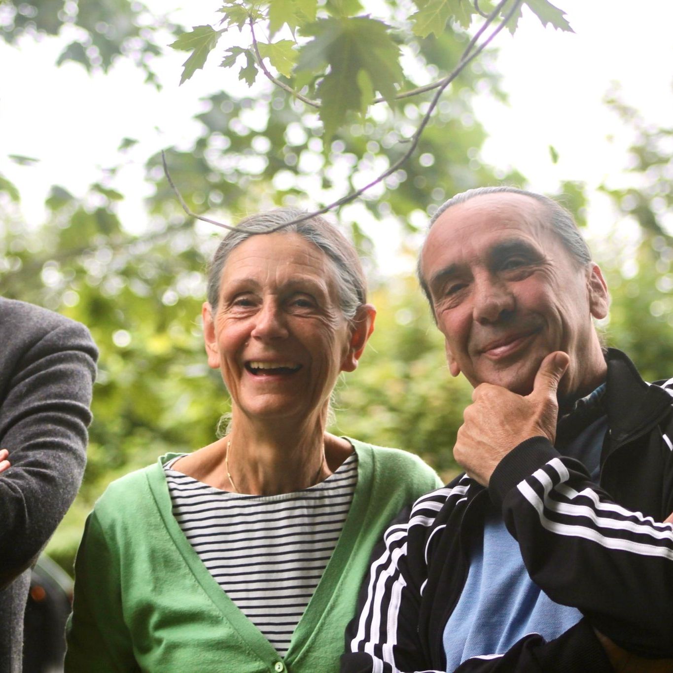 Three older adults smiling and standing outdoors, with trees in the background.