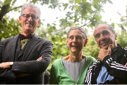 Three older adults smiling and standing outdoors, with trees in the background.