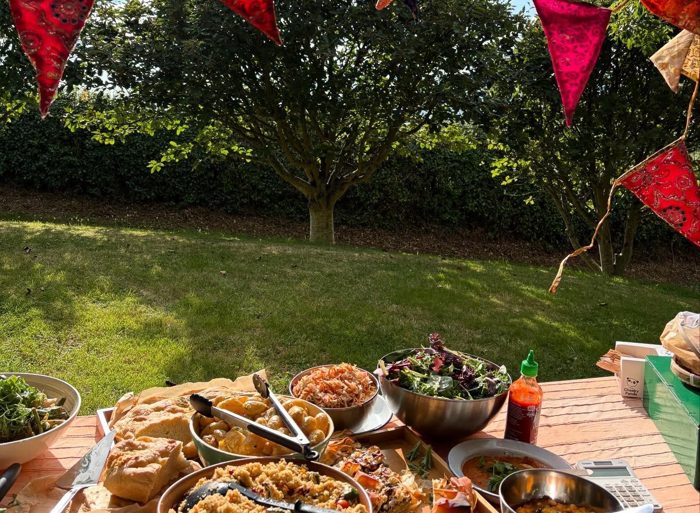Outdoor picnic table with various dishes, under a canopy with colorful bunting flags.