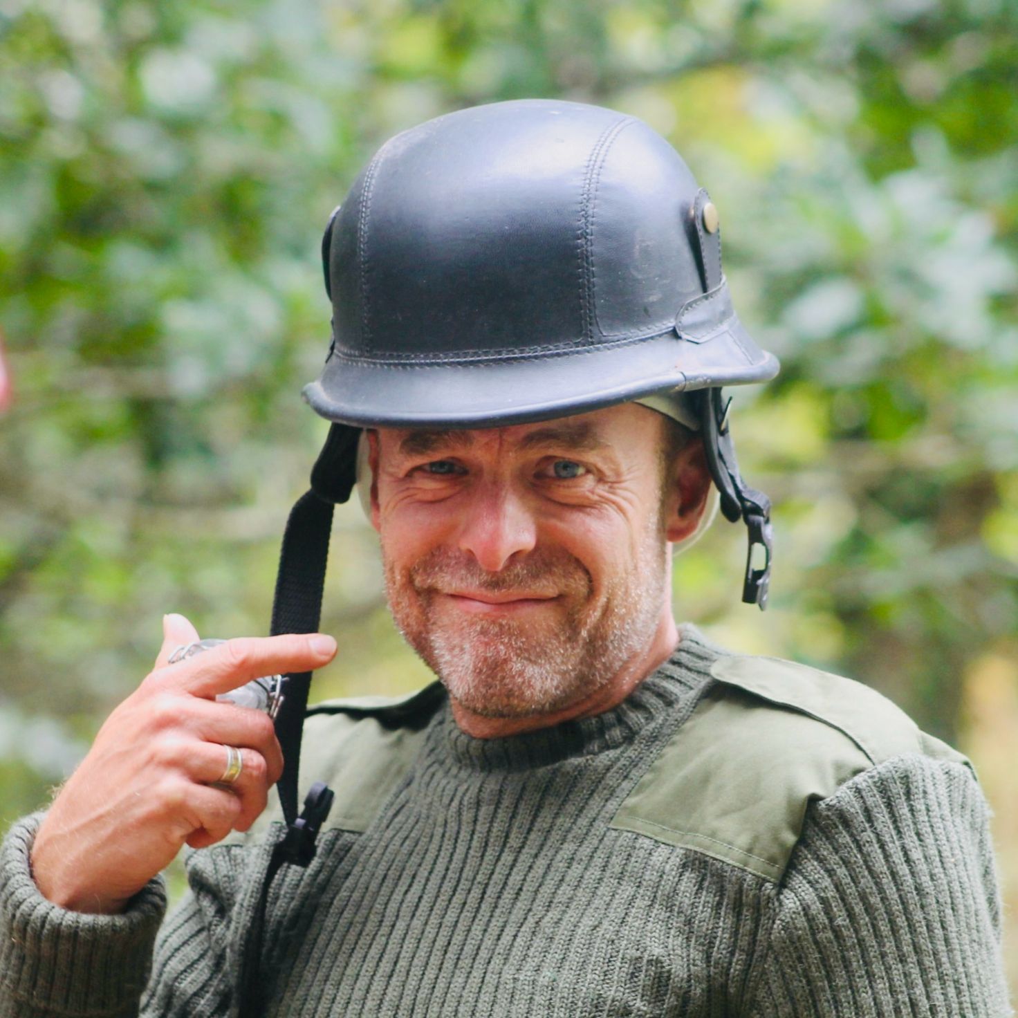 Man wearing a helmet and green sweater smiling outdoors