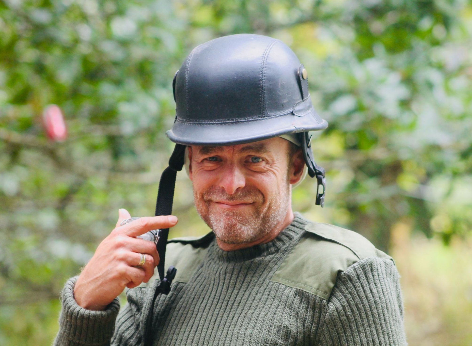 Man wearing a helmet and green sweater smiling outdoors