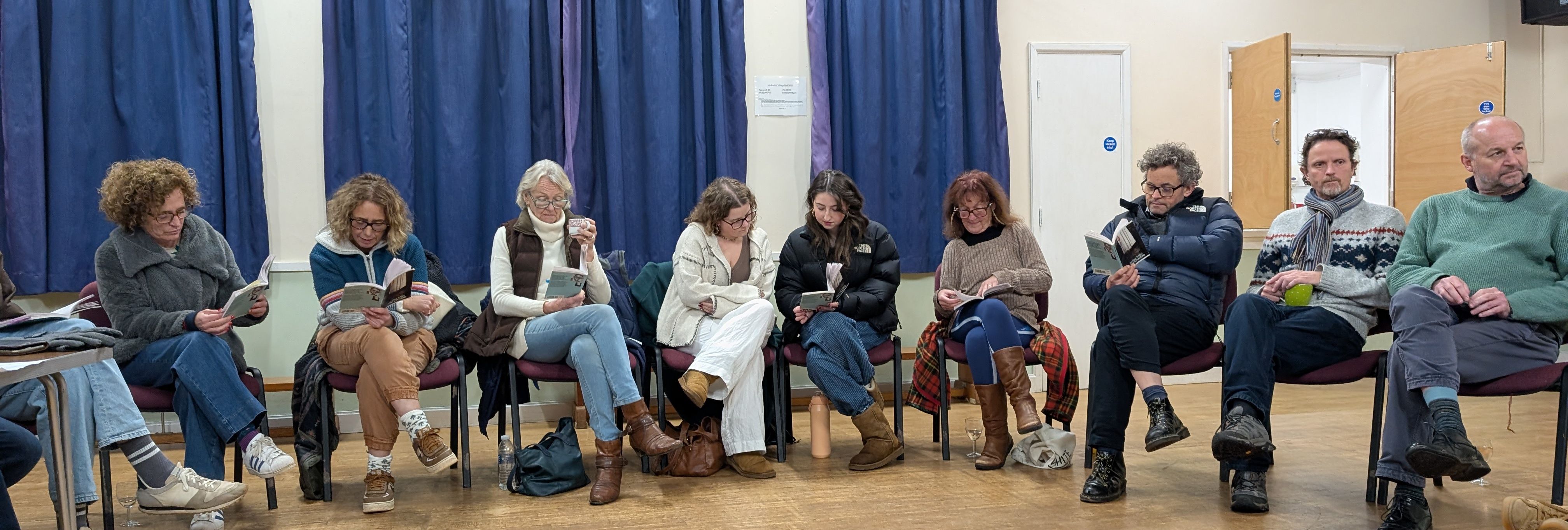 A group of people sitting in a circle reading books in a community hall.