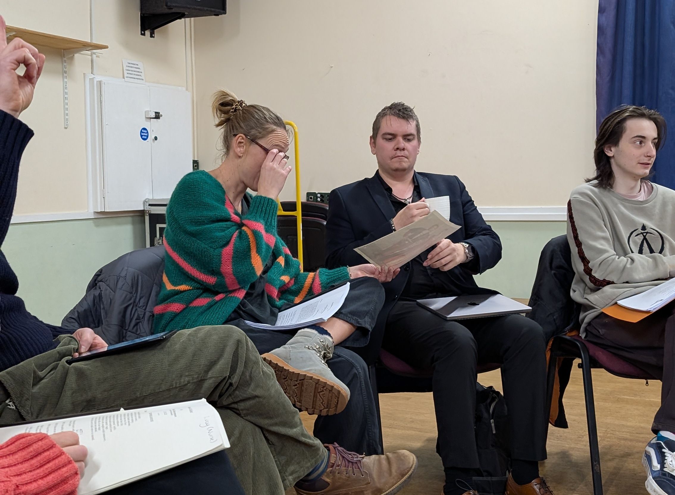 Group of people sitting in a circle, reading or discussing papers in a room.