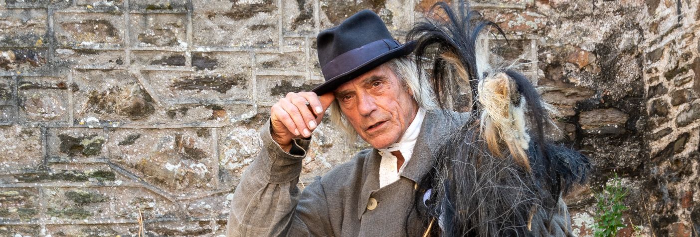 Man in traditional costume posing with one foot up on a stone wall