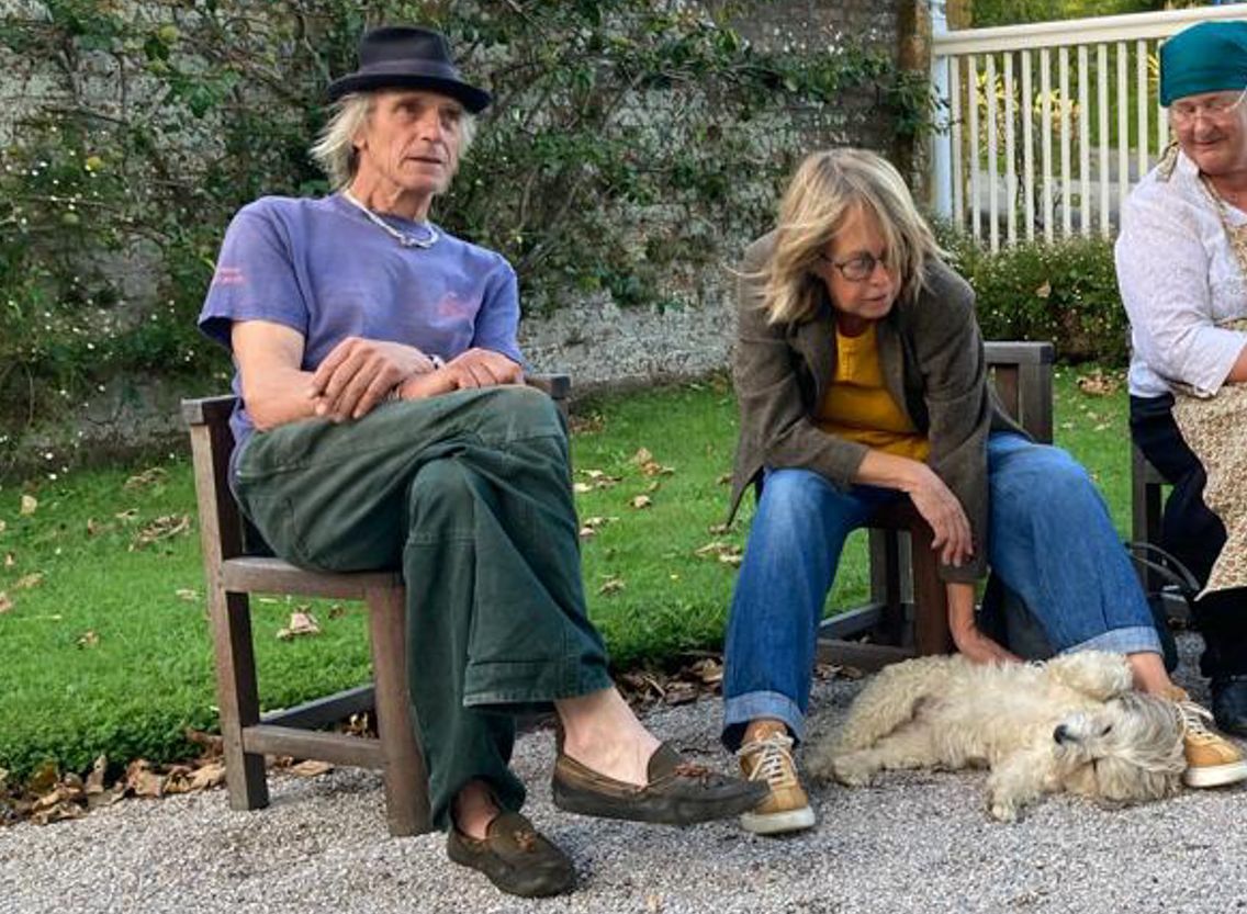 People sitting outdoors on chairs with a dog lying on the ground between them.