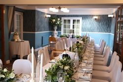 Wide view of wedding dining table with Green and white flower arrangements, champagne, and wedding cake in the background