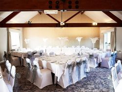 Wide view of wedding dining room with White table and chairs with silver bows and white feather centre pieces