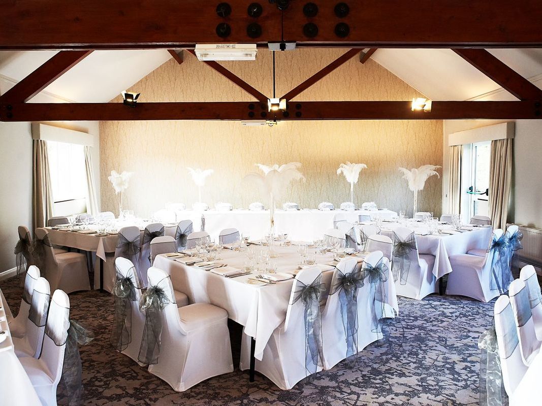 Wide view of wedding dining room with White table and chairs with silver bows and white feather centre pieces